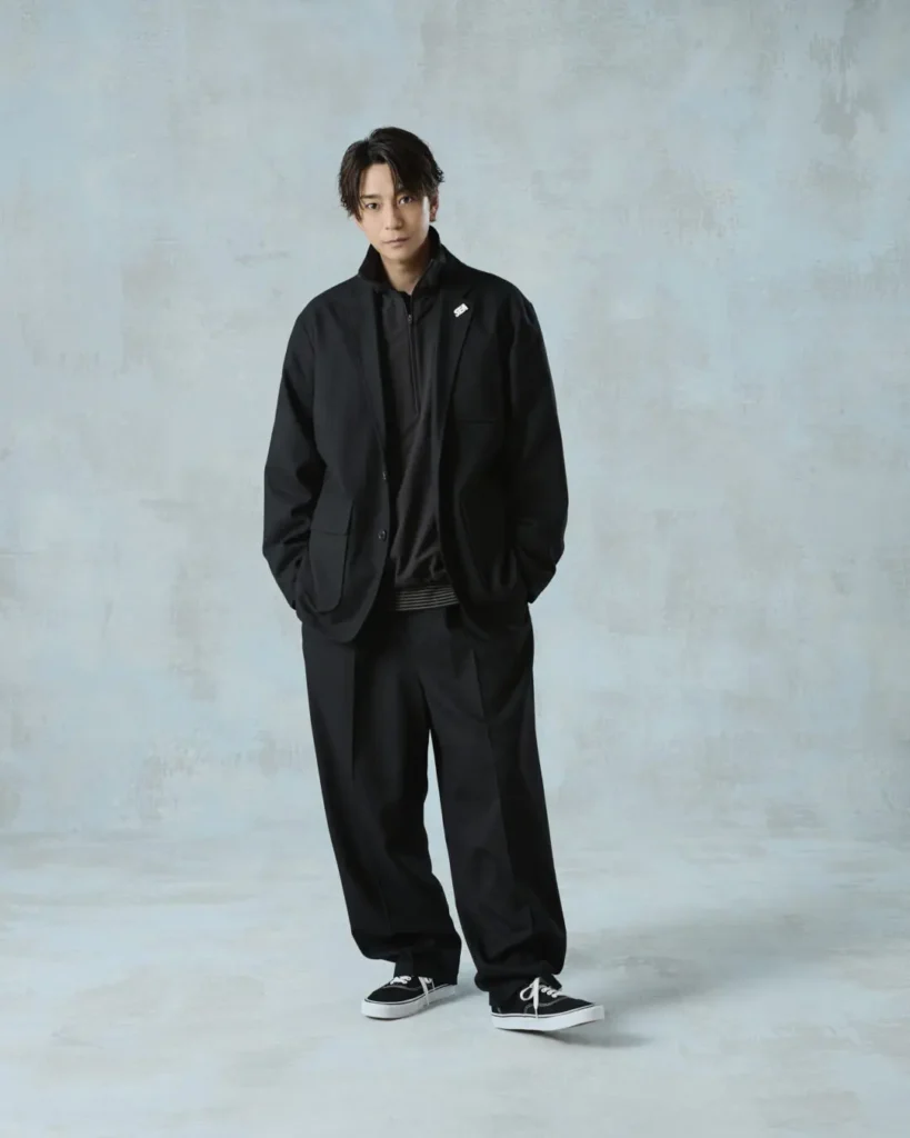 Full-body portrait of the model wearing a black tailored jacket layered over casual separates with black shoe
