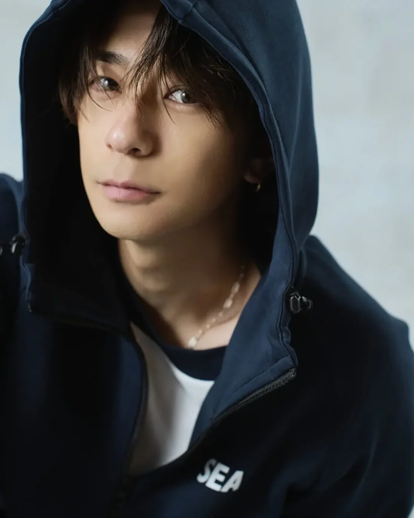 Close-up portrait of the model wearing a navy hooded zip-up with the hood up and a small "SEA" logo on the chest