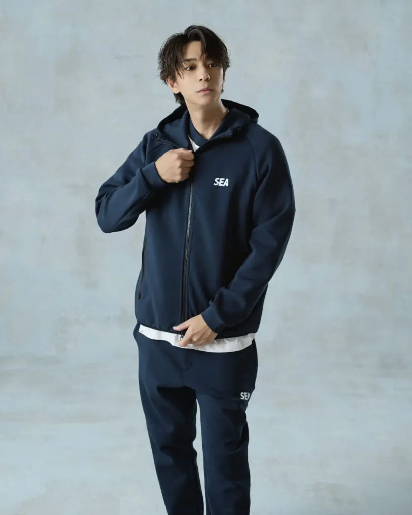 Model wearing a navy "SEA" zip-up hoodie and matching joggers over a white T-shirt in a relaxed standing pose