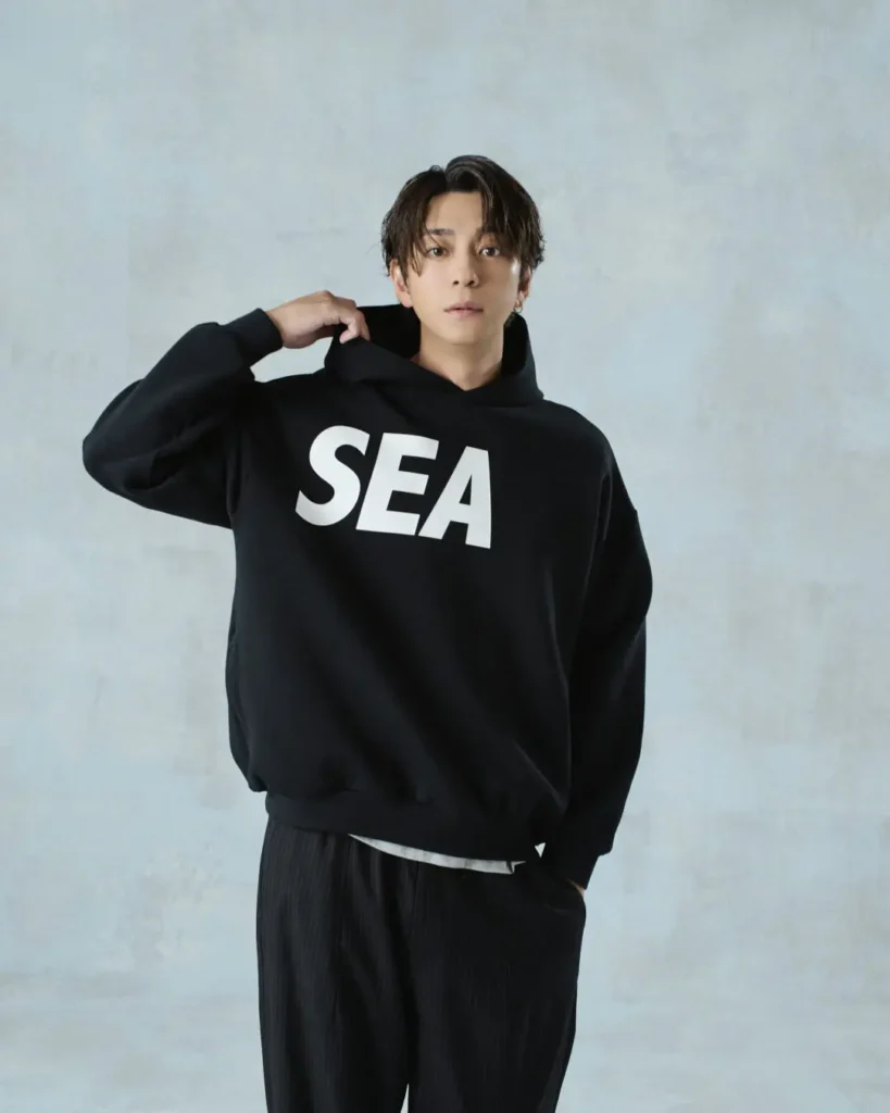 Front-facing portrait of the model wearing a black hoodie with oversized white "SEA" lettering across the chest