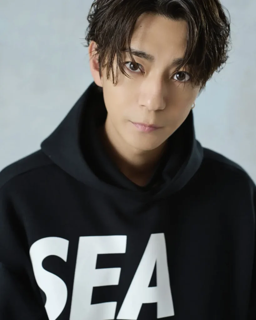 Close-up portrait of the model in a black "SEA" hoodie with a calm expression against a light blue studio backdrop