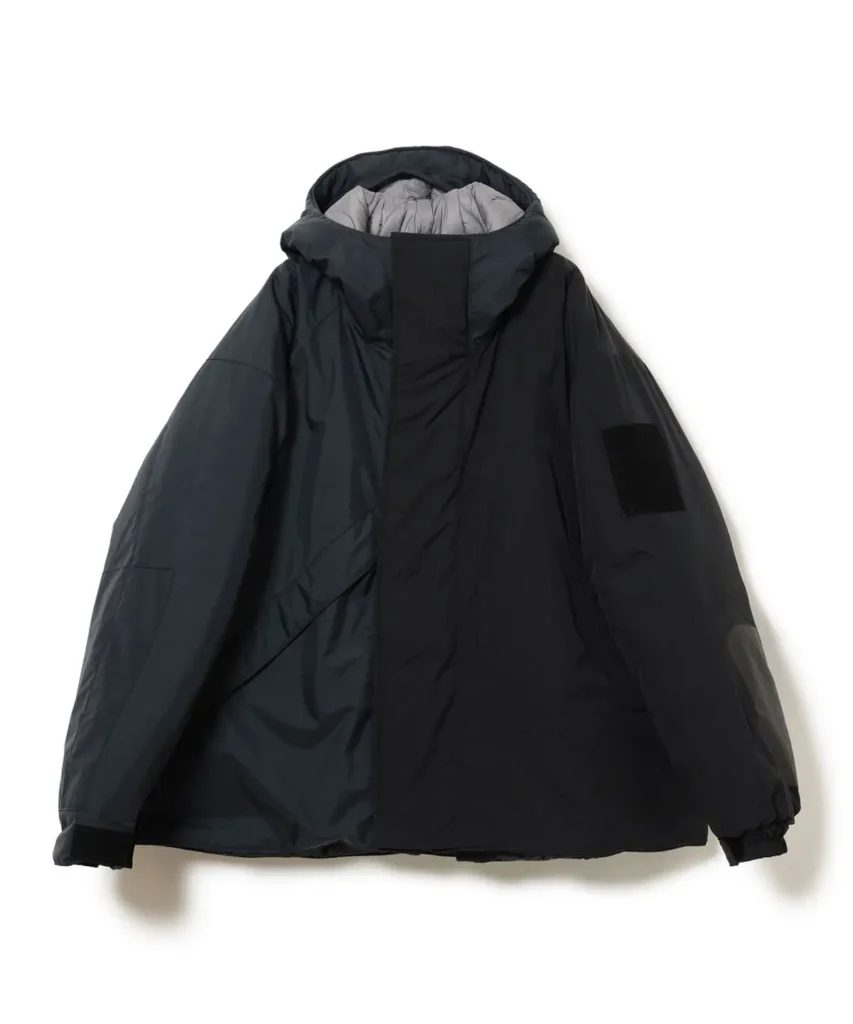 Black oversized hooded technical jacket with a high protective collar, concealed front closure, relaxed sleeves, and tonal utility patch