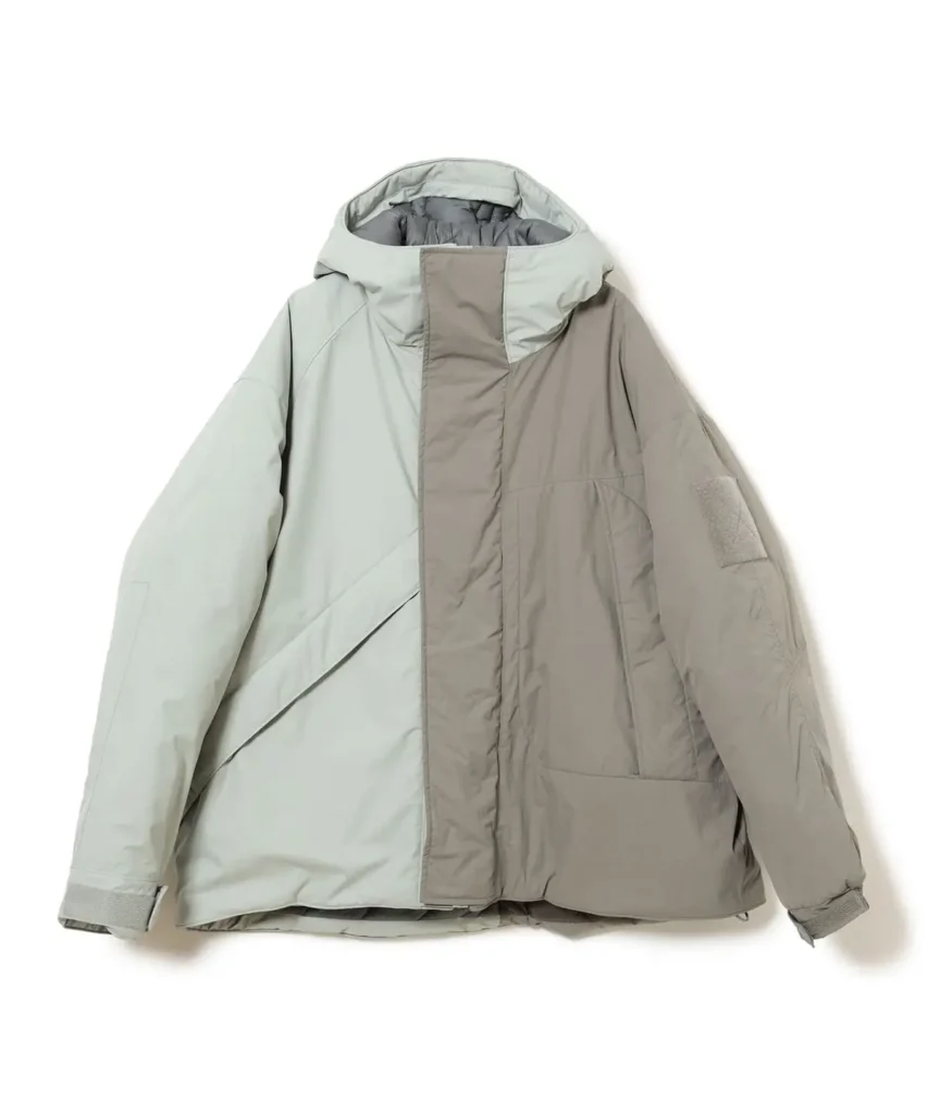 Two-tone pale gray and taupe hooded technical jacket with an asymmetrical panel design, oversized fit, concealed closure, and utility detail