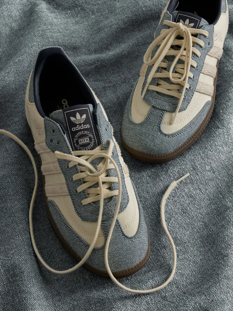 Two blue-gray and cream Adidas sneakers with beige laces on textured gray fabric