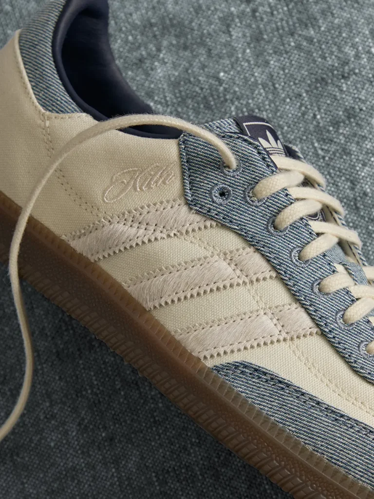Close-up of a beige Adidas sneaker with frayed three stripes, blue denim-style eyelet panel, cream laces and gum sole on