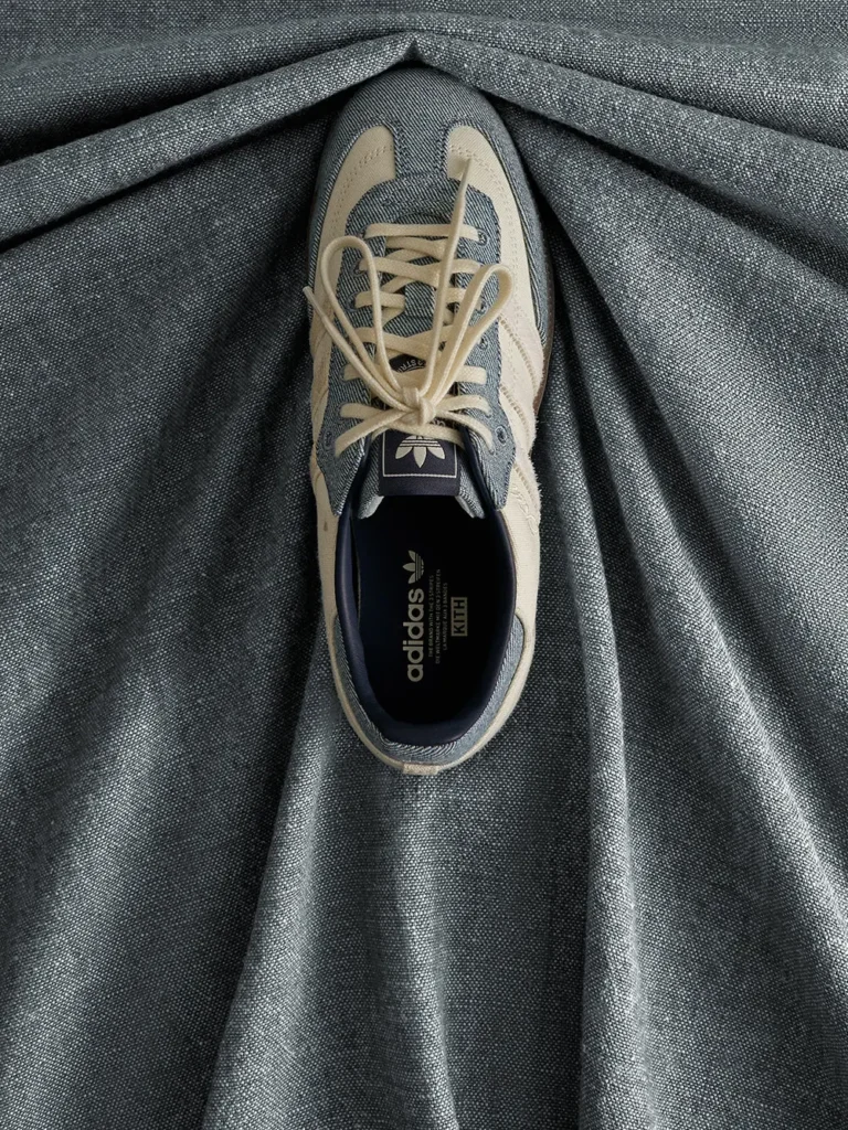 Beige and gray Adidas sneaker with cream laces resting on pleated dark gray fabric