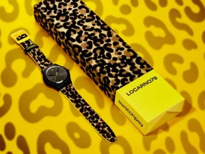 Lifestyle product composition showing the leopard-print Swatch watch alongside its matching patterned box on a bold yellow leopard-print surface