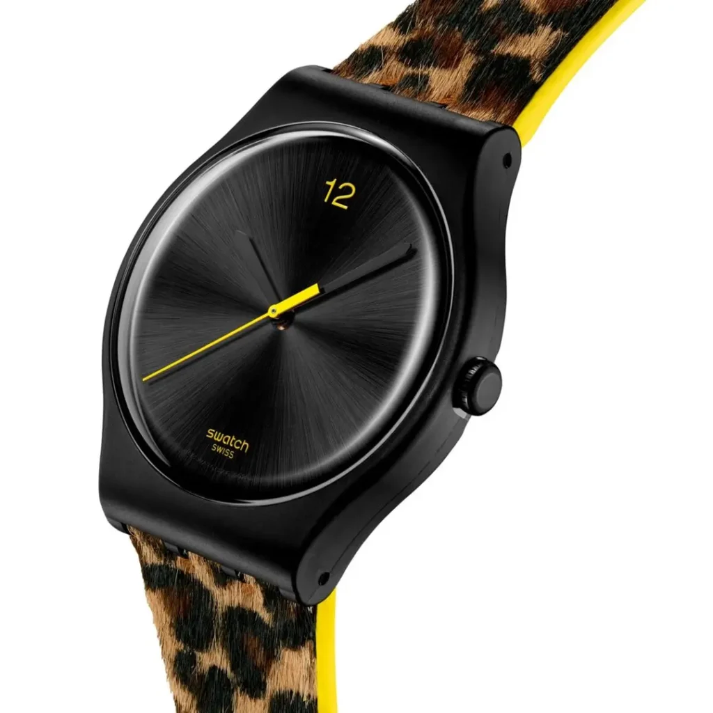 Angled three-quarter view of the Swatch watch highlight the black case, brushed black dial, yellow accents, and textured leopard-print strap against a clean white backdrop