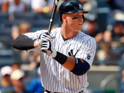 Aaron Judge, Yankees batter readies his swing during a sunlit game, focused on the incoming pitch before a packed crowd