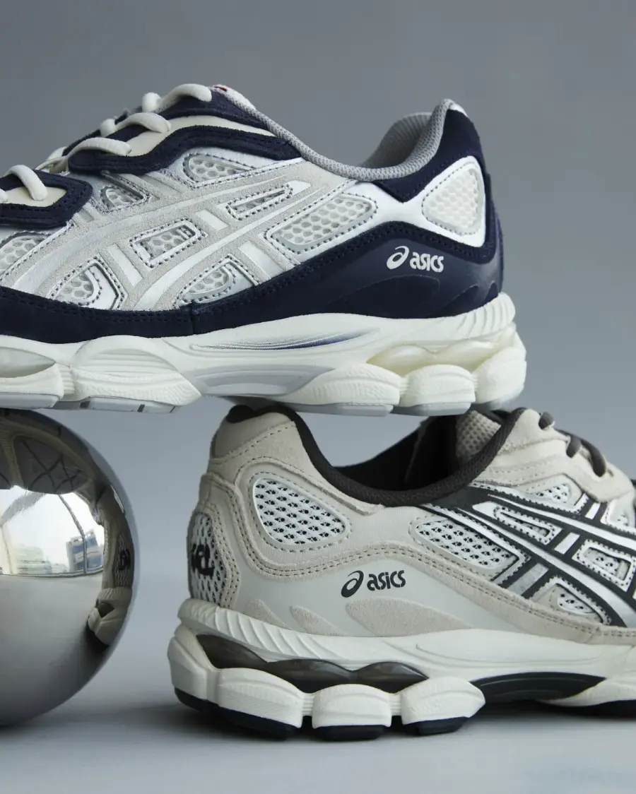 Two ASICS running sneakers in contrasting white-and-navy and white-and-black colorways, stacked above a reflective chrome sphere to showcase their breathable mesh uppers and sculpted midsoles.