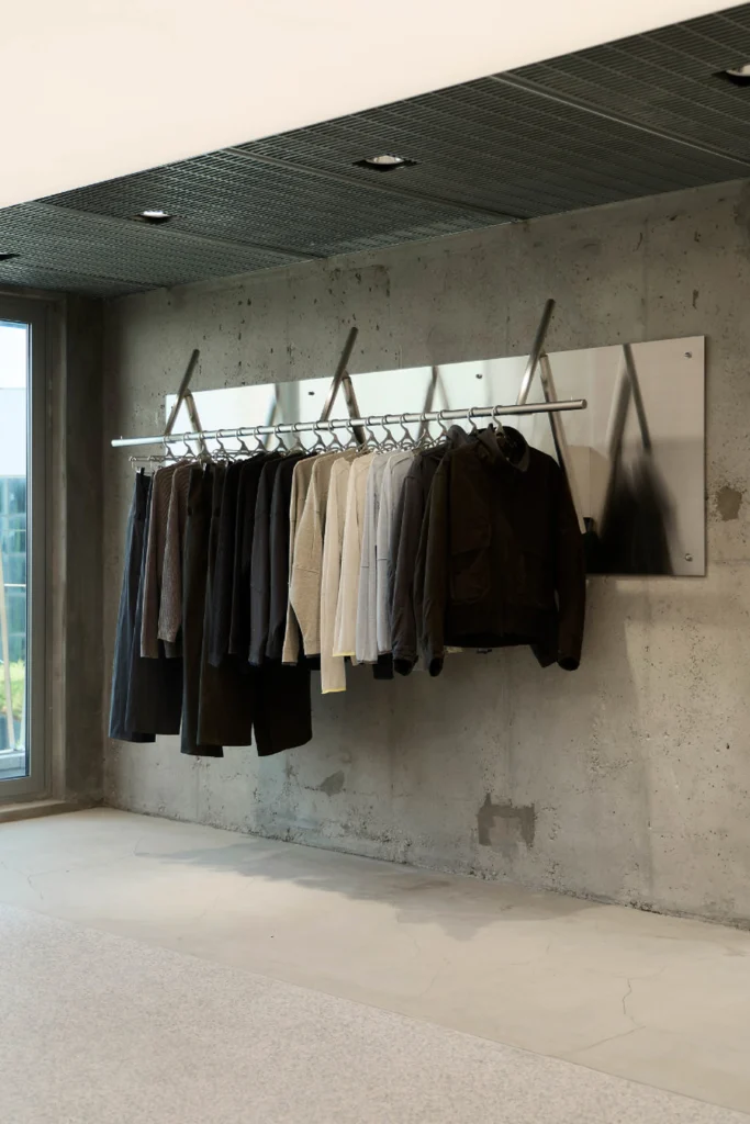 Neutral Clothing Collection Hanging On Metal Rail Against Concrete Wall