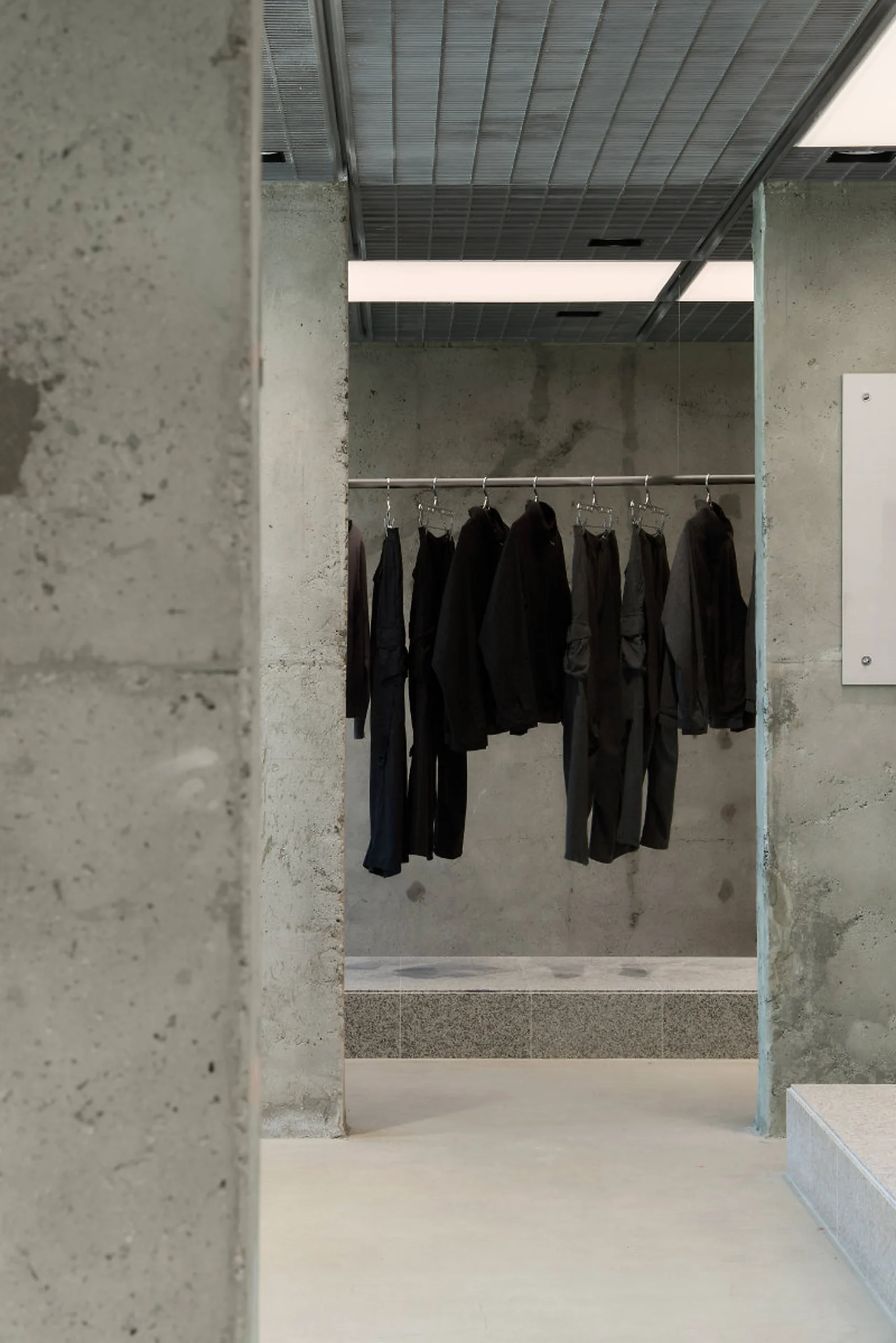 Dark Garments Hanging In Concrete Alcove Beneath Grid Ceiling