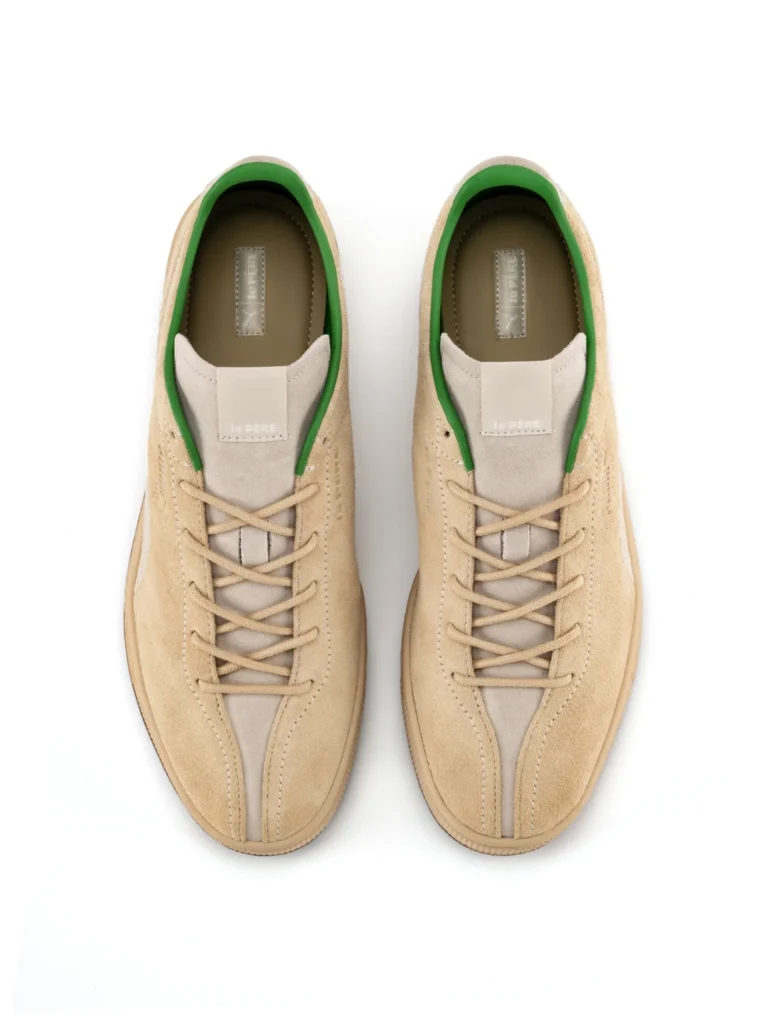 A direct top-down view of the PUMA x le PÈRE Suede shoe show the beige suede upper and the "le PÈRE" brand deboss on the tongue. The split-toe design create a distinct seam at the toe box, and the contrast green inner line is highly view around the collar