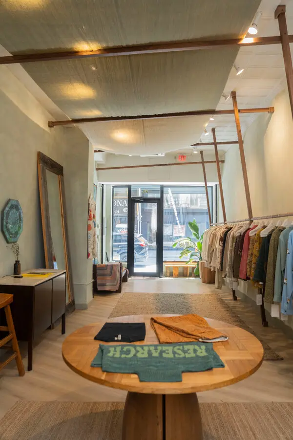 Kartik Research boutique interior with clothing racks, a round wooden display table, rugs, and natural light.