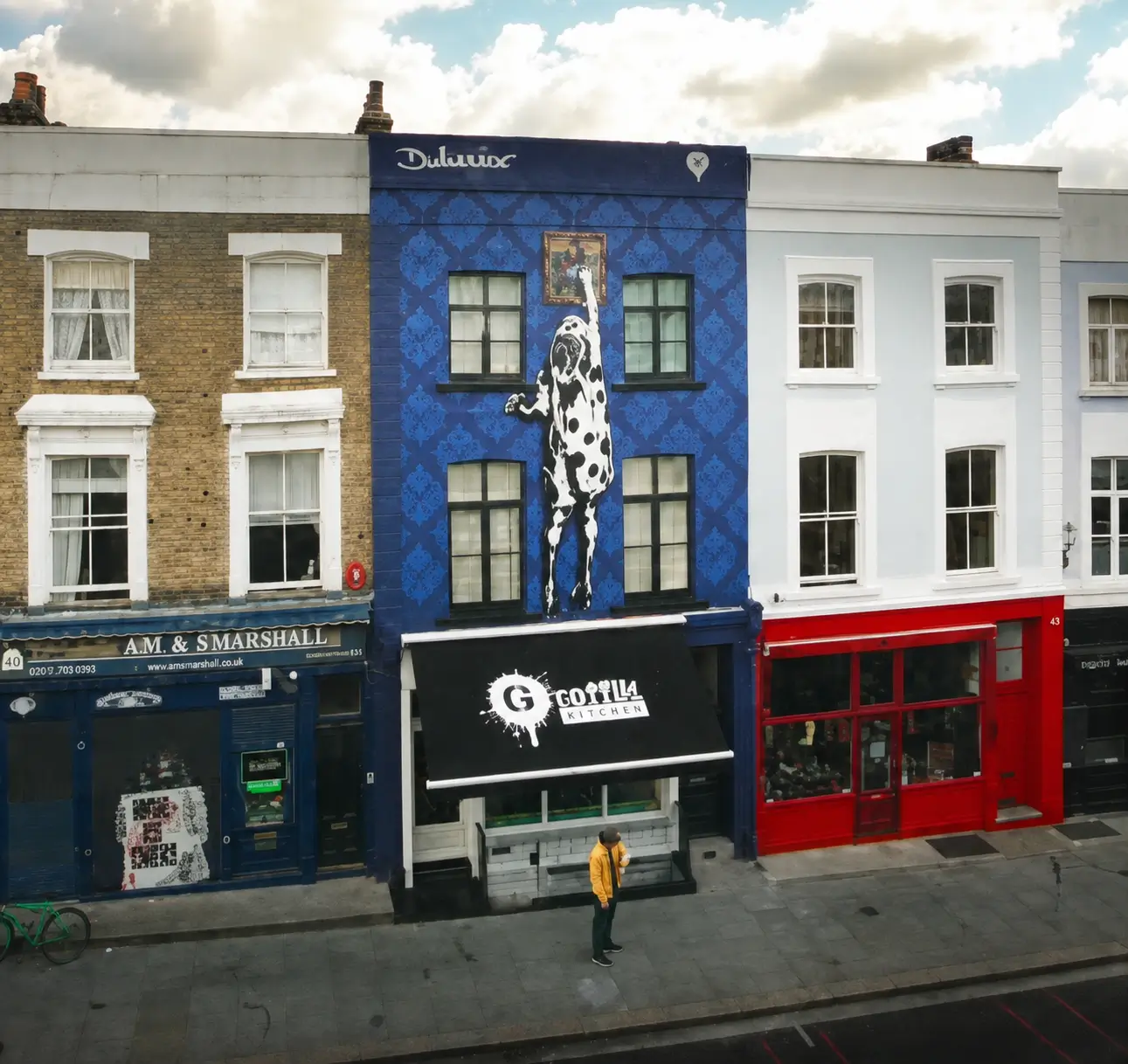 Blue-painted London storefront featuring a large black-and-white cow mural reaching toward a framed artwork above Gorilla Kitchen.