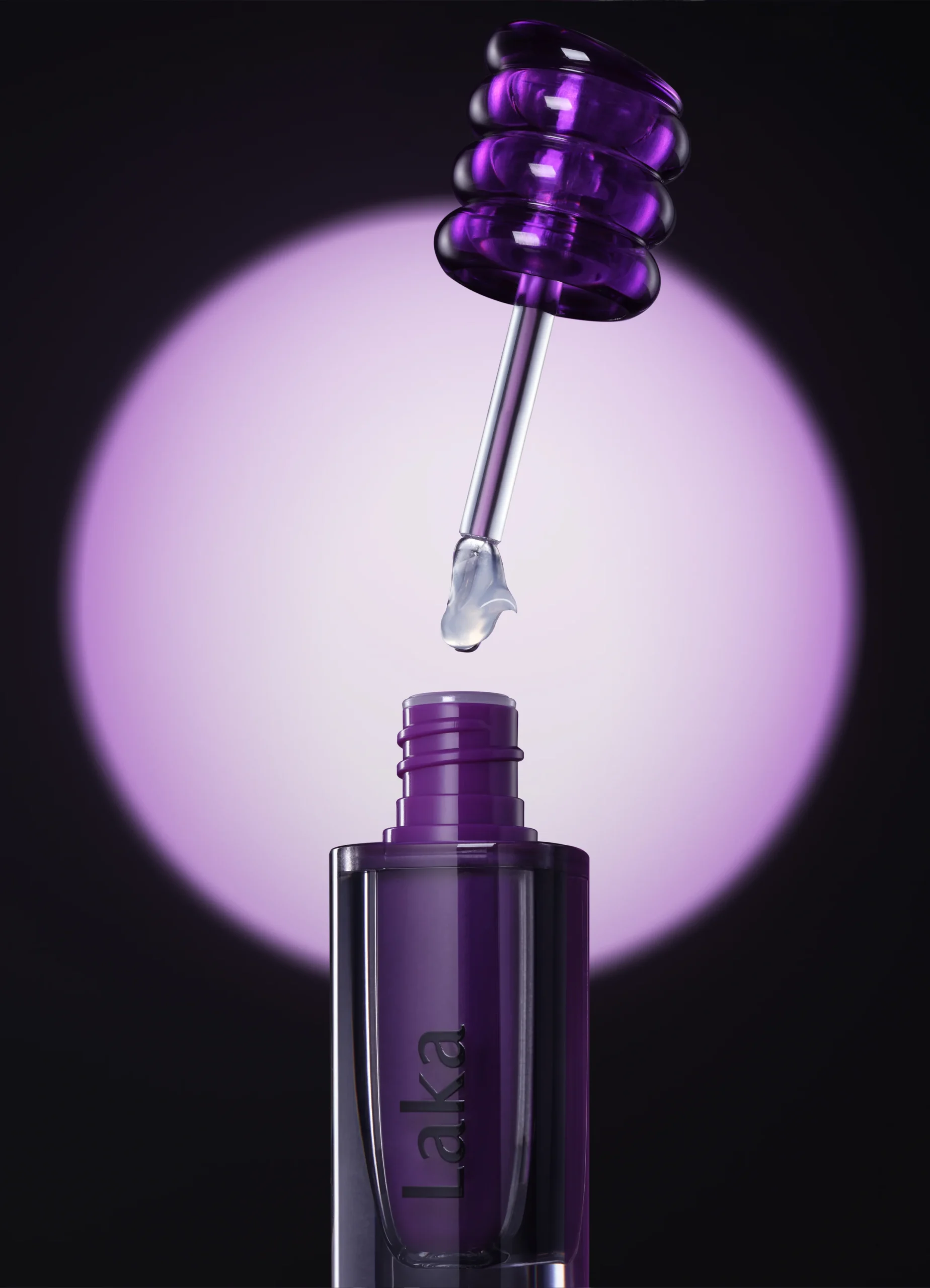 Laka purple lip product with sculptural cap and clear applicator suspended above the open bottle against a glowing violet backdrop.