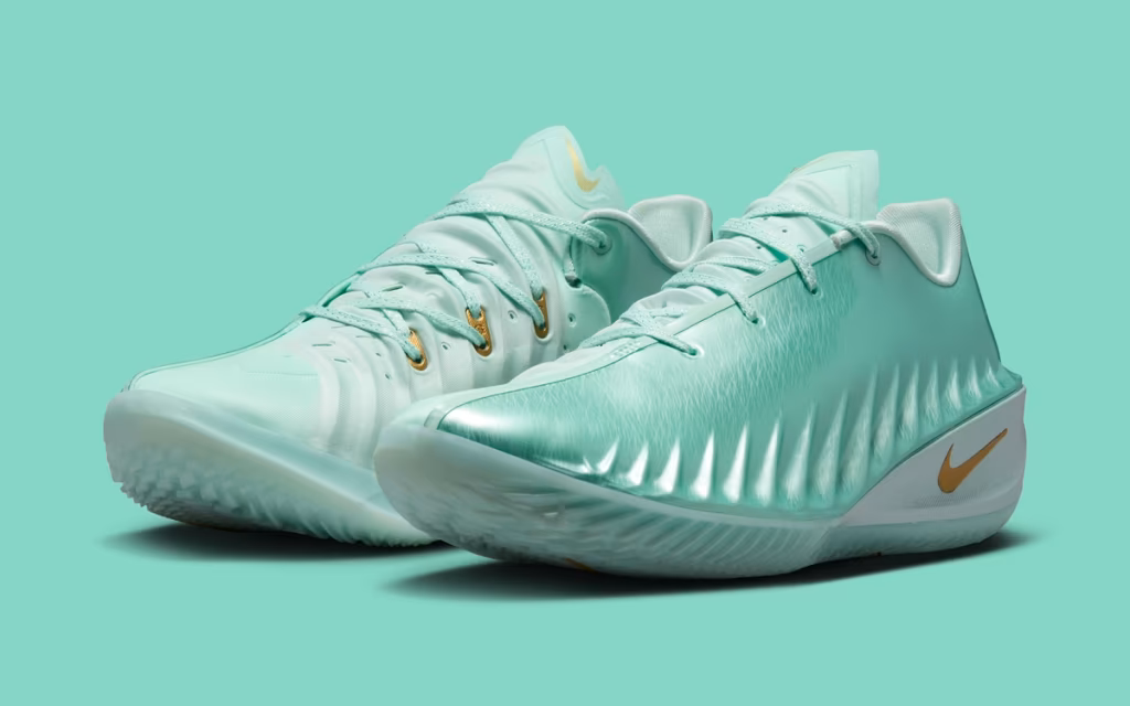Mint green Nike low-top basketball shoes with metallic gold Swooshes, sculpted sidewalls, and translucent outsoles displayed against a matching pastel green background.