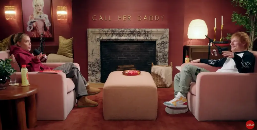Podcast Interview Inside The Call Her Daddy Studio With Two Guests Seated Across From Each Other In Pink Armchairs Beside A Marble Fireplace