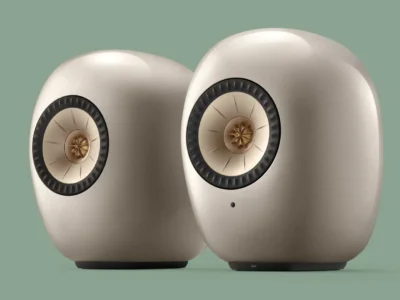 Pair of KEF LSX II LT wireless bookshelf speakers in matte cream, shown against a soft sage-green background with the brand's signature Uni-Q concentric driver prominently display
