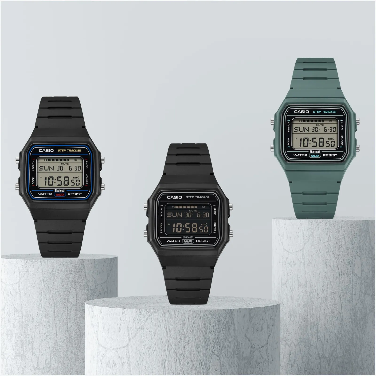 Three Casio digital watches in black and green displayed on white textured pedestals