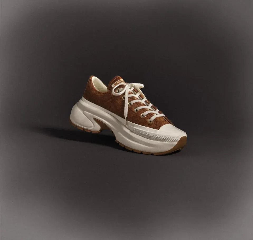 Brown textured Converse platform sneaker with a chunky white sole and gum outsole displayed against a dark gradient studio background.