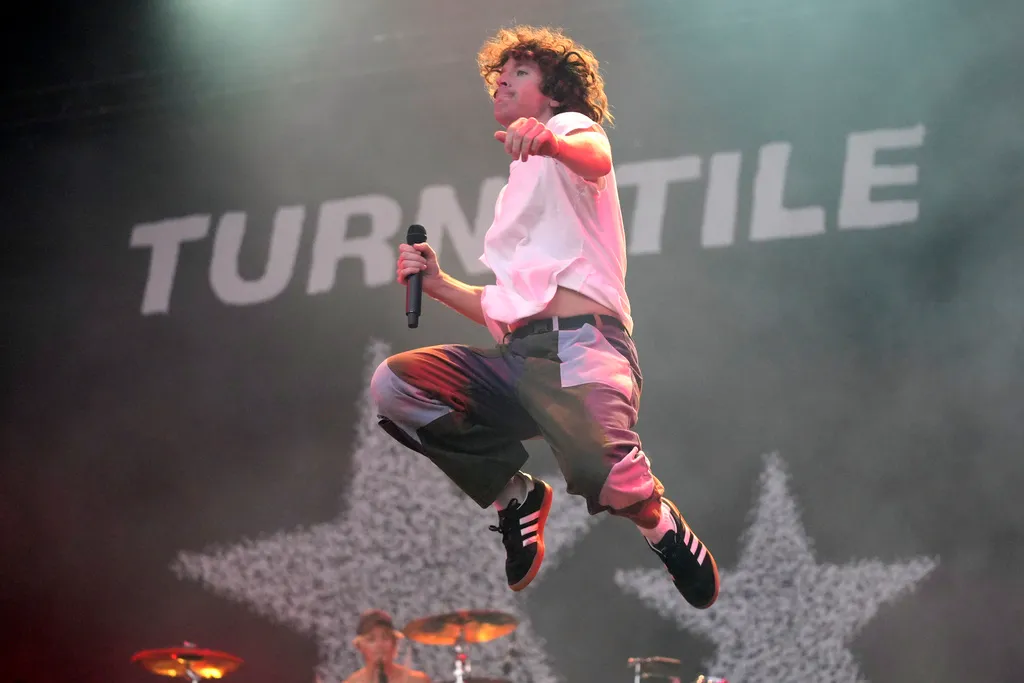 Turnstile singer Brendan Yates leaps across the stage with a microphone during a concert performance