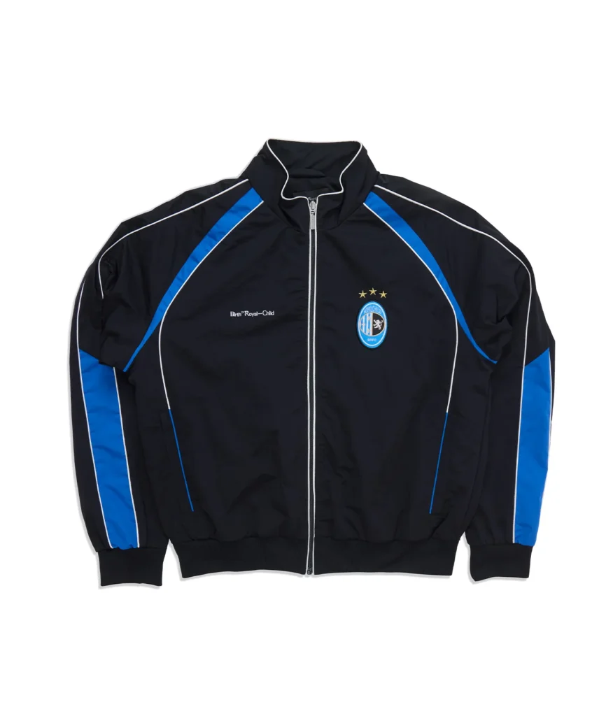 Black zip-up track jacket with royal blue paneling, white piping, embroidered Birth®RoyalChild logo, soccer-inspired crest with three stars, ribbed cuffs, and stand collar