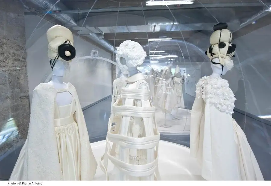 White sculptural Comme des Garçons garments and elaborate headpieces displayed inside a transparent exhibition dome.