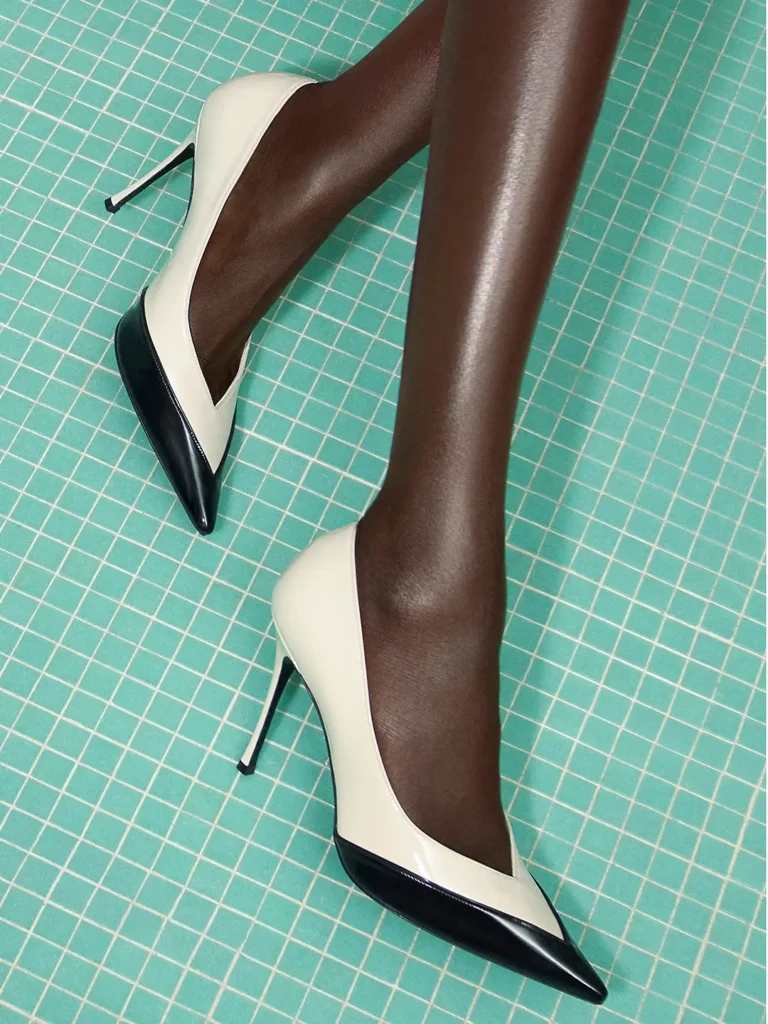 Close-up of cream-and-black pointed Ferragamo pumps with slim stiletto heels against a turquoise mosaic tile floor