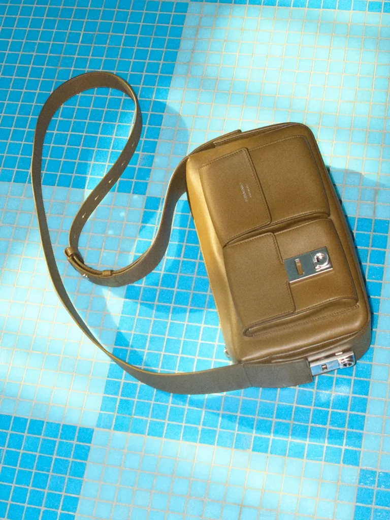 Olive green Ferragamo crossbody bag with silver-tone hardware and oversized adjustable strap photographed on a bright blue tiled pool deck