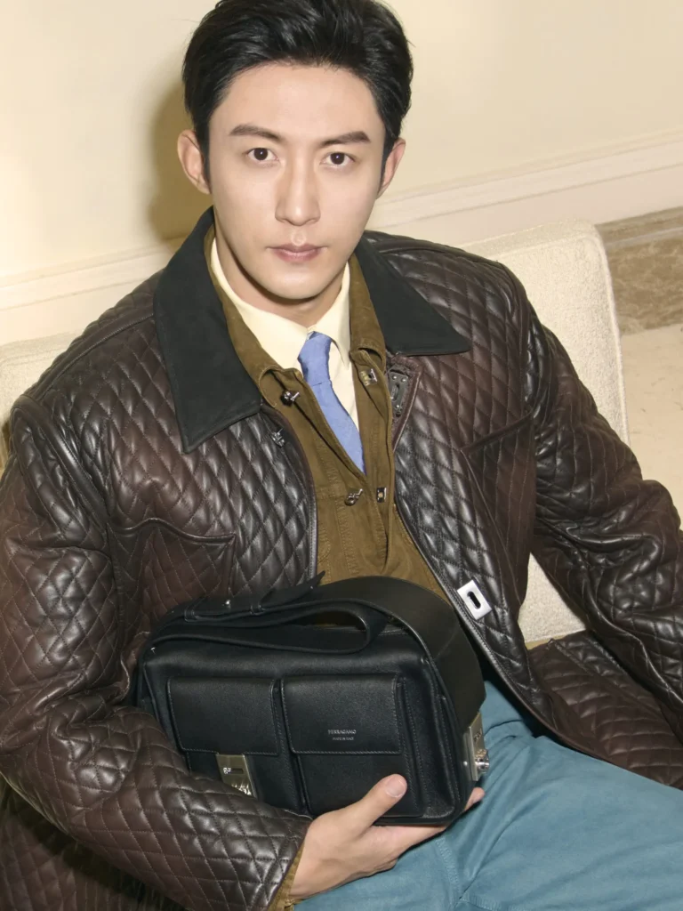 Portrait of a male model in a brown quilted leather jacket layered over tailored separates while holding a black Ferragamo utility-inspired leather bag