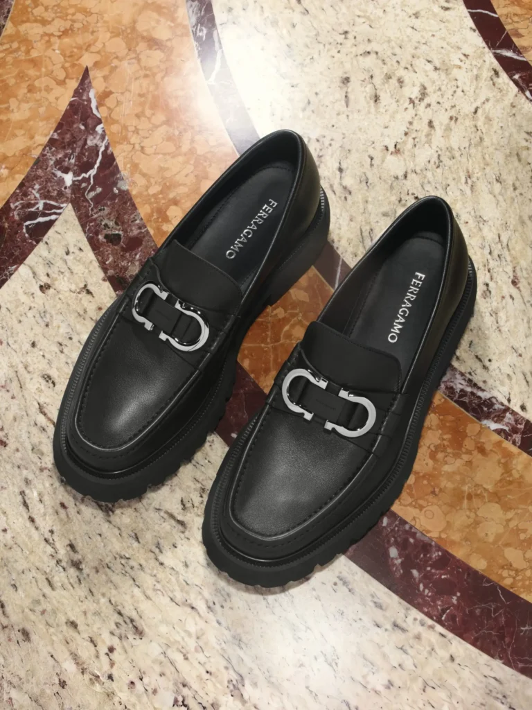 Pair of black leather Ferragamo chunky loafers featuring oversized silver Gancini horsebit hardware and rugged lug soles displayed on patterned marble floor