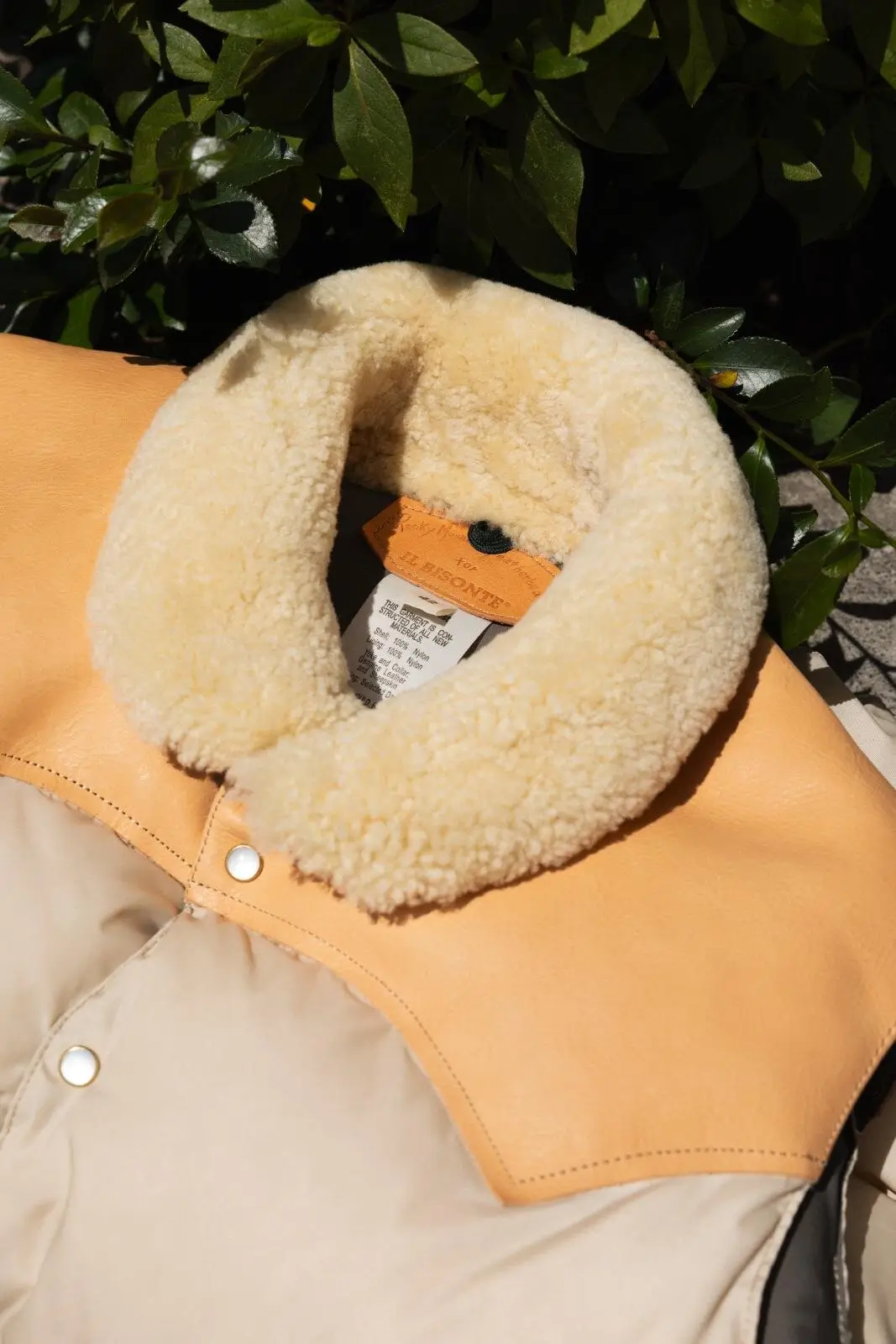 Close-up of the shearling collar and leather yoke on the IL BISONTE x Rocky Mountain Featherbed down vest, showing the co-branded hang tag stitched into the seam