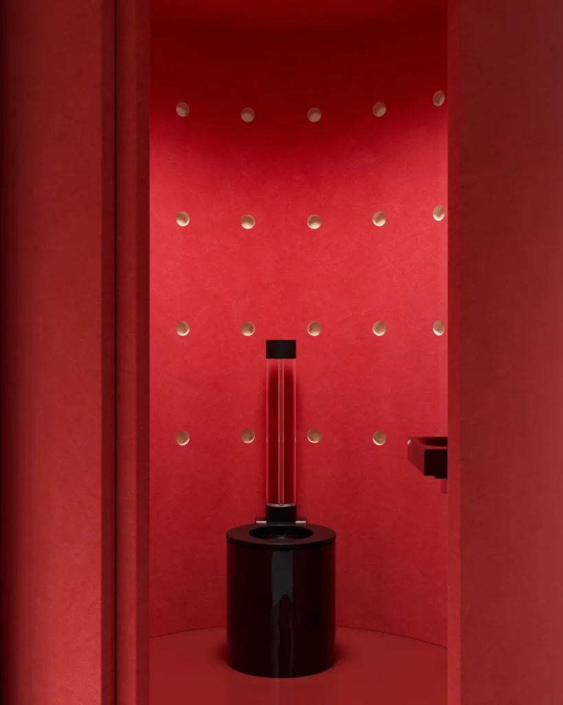 Monochromatic red bathroom with textured walls, circular recessed details, and a sculptural black cylindrical toilet accented by a transparent flush column