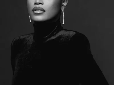 Monochrome studio portrait of Keke Palmer wear a dark velvet turtleneck, sleek side-parted hair, dramatic eye makeup, and long drop earrings against a dark background