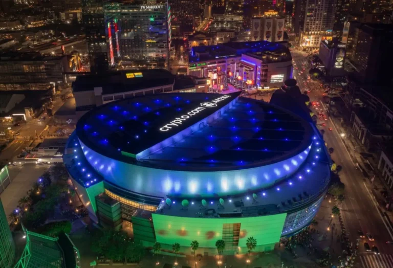 Aerial Night View Of Crypto.com Arena In Downtown Los Angeles, Show With Blue And Green Lights And Surrounded By City Buildings, Streets, And Traffic