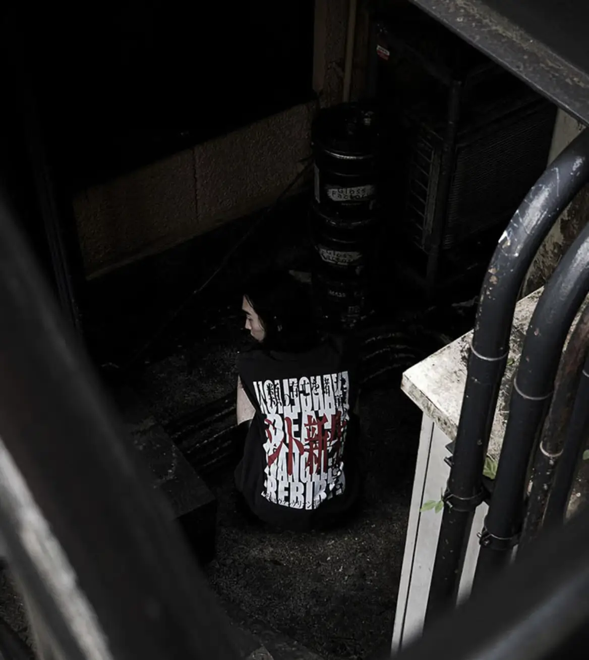 Person in a Graphic Black T-Shirt Stands in a Dark Industrial Stairwell