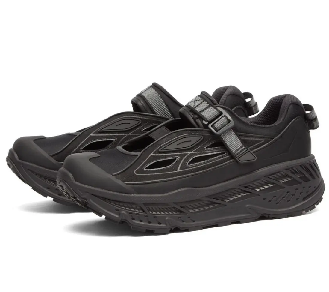 Pair of black HOKA trail shoes with adjustable strap closures, cutout side panels, protective toe caps, and oversized cushioned midsoles.