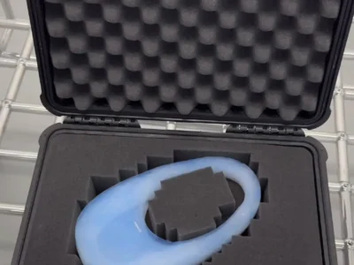 Open hard-shell case with custom foam insert holding a smooth, translucent blue sculpture object