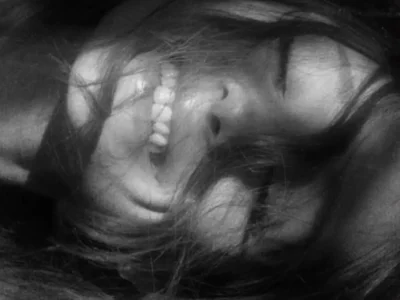 Black-and-white close-up portrait of a smiling Ariana Grande lying on their side with long hair partially covering their face, creating a soft, intimate, and dreamy composition