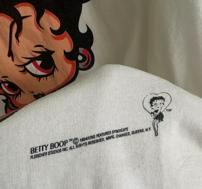 Close-up of a vintage Betty Boop graphic T-shirt showing the official copyright print, a miniature Betty Boop illustration, and a larger character graphic in the background on soft white cotton fabric.