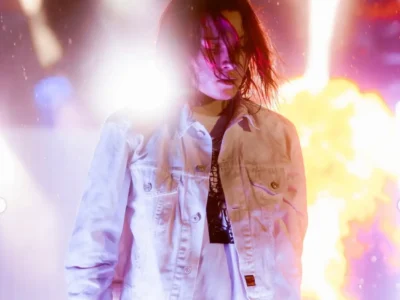 Nettspend in a white jacket standing against a backdrop of fire, haze, and vivid stage lights, creating a cinematic concert portrait