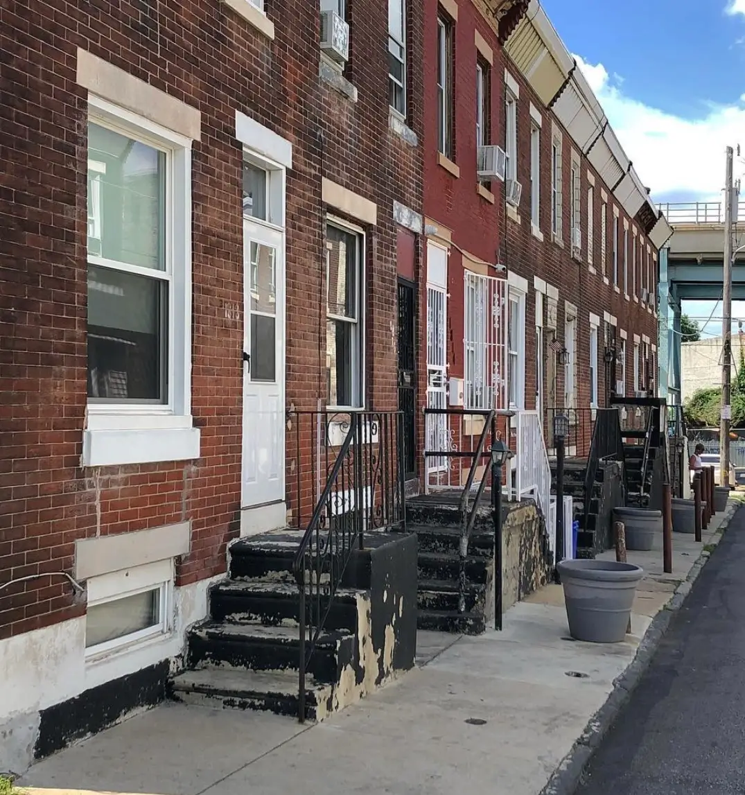 Row of red-brick Philadelphia rowhouses with front stoops along a narrow residential street.