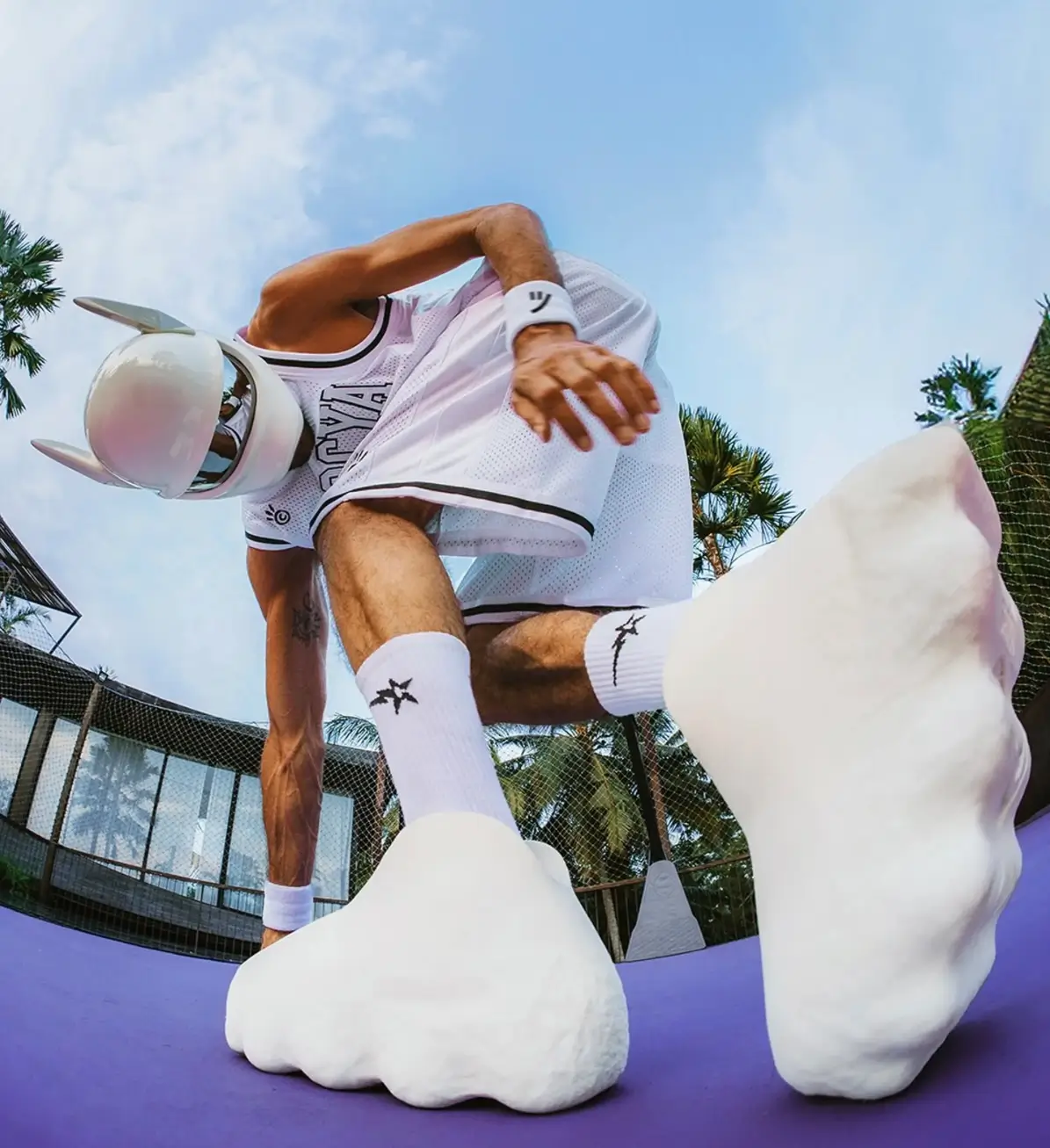 Low-angle campaign image of a person in white sportswear and a futuristic helmet wearing oversized white Mars Mellow footwear on a purple court.
