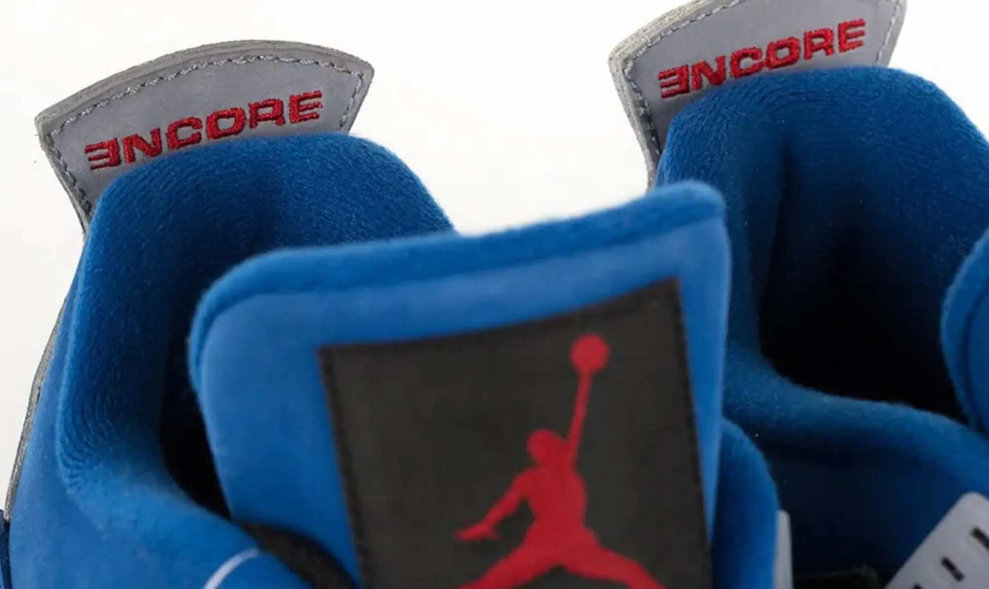 Close-up of blue Air Jordan 4 sneakers showing padded tongues, red Jumpman branding, and gray heel tabs embroidered with ENCORE in red.