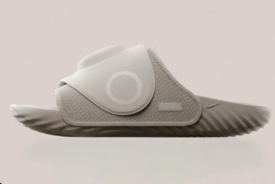 Light gray Nike Air Zoom Hyperslide recovery slide shown in side profile, featuring a wide cushioned strap, breathable mesh construction, circular Hyperice detail, subtle Nike Swoosh, and sculpted ripple sole.