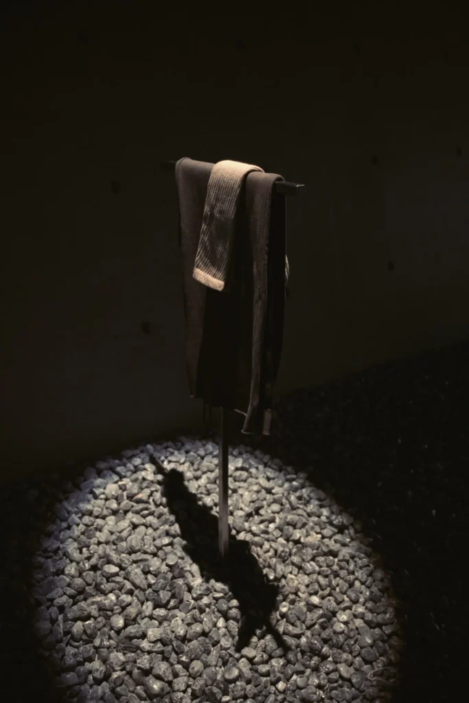 Dark Knit Garment Drape Over Min Display Stand Above Gray Stones Under A Focus Spotlight