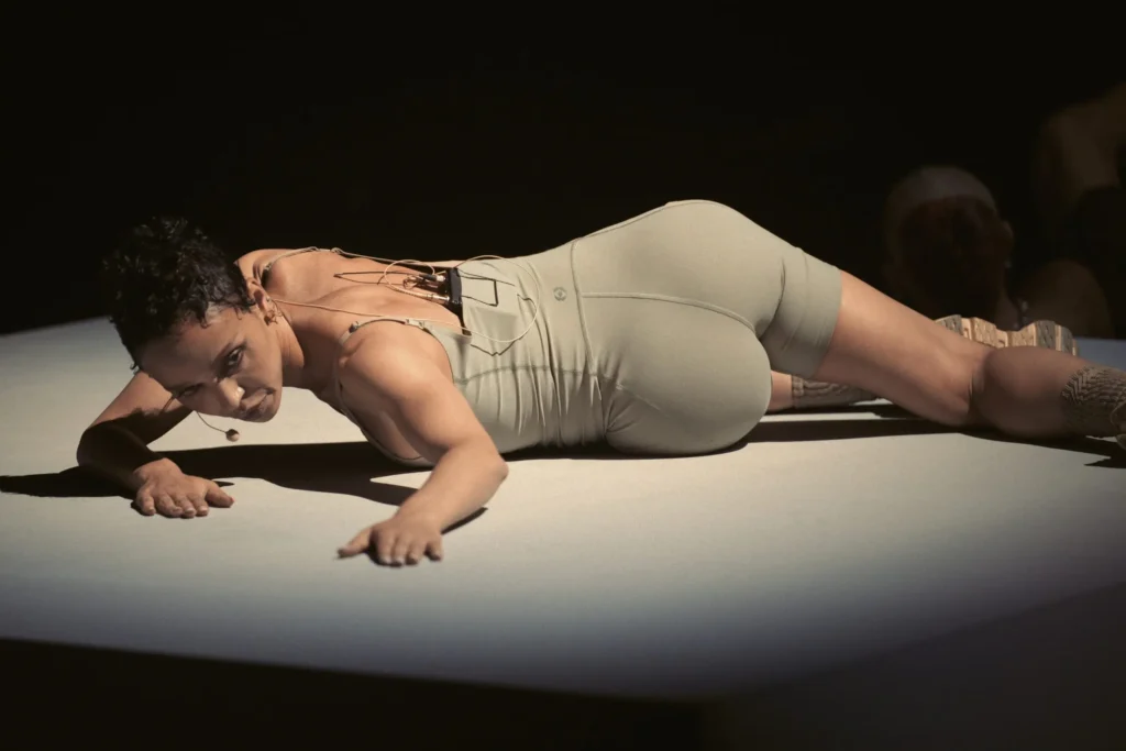 Performer In Neutral Fitted Clothing Recline On A Raise Platform Wear A Headset Microphone