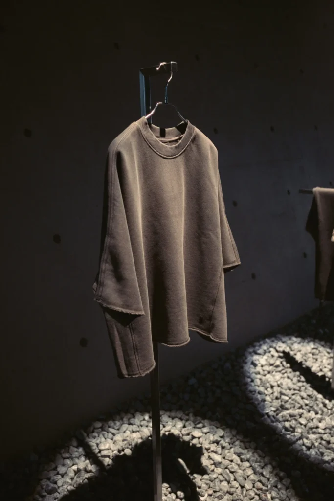 Oversize Dark Knit Top Display On A Min Stand Above Gray Stones Under Drama Light