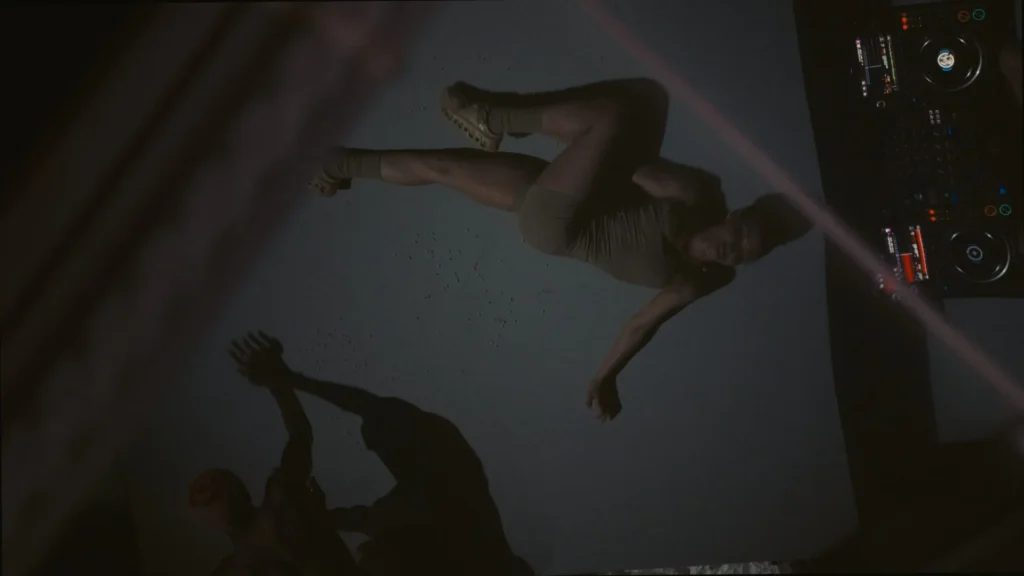 Overhead View Of Two Performer Move Across A Dimly Lit Stage Beside DJ Equipment